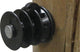 Close-up of a black Dare Elfin Wood Post Insulator mounted on a wooden surface.