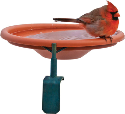 A cardinal perches on the rim of a terracotta deck mount birdbath with a teal stand.